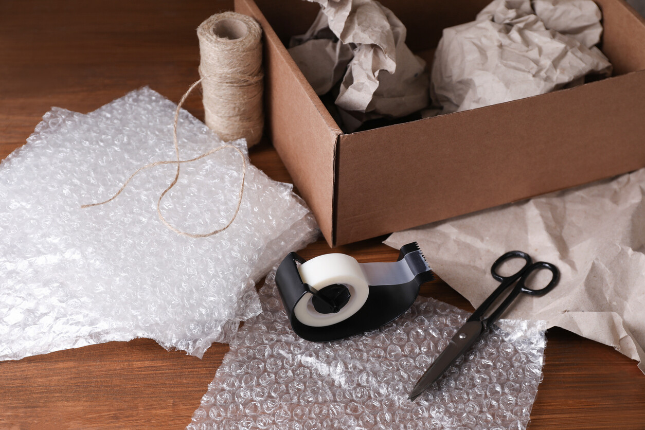 Open cardboard box with packing supplies on a wooden table. - how to pack glasses for moving