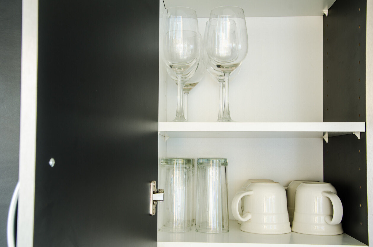 Wine glasses, tumblers, and ceramic mugs stored on white shelves. - how to pack glasses for moving