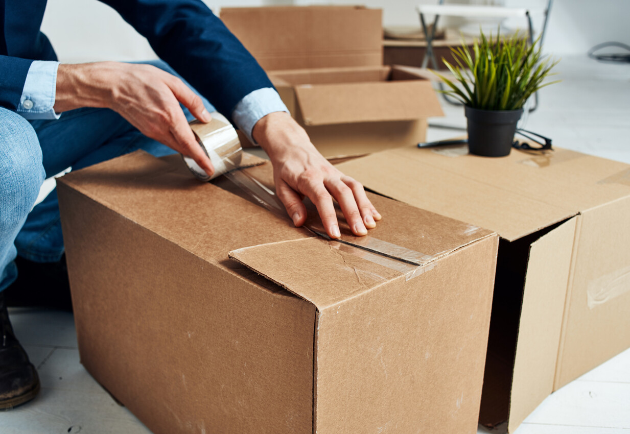 Person sealing a cardboard box with clear packing tape. - how to pack glasses for moving