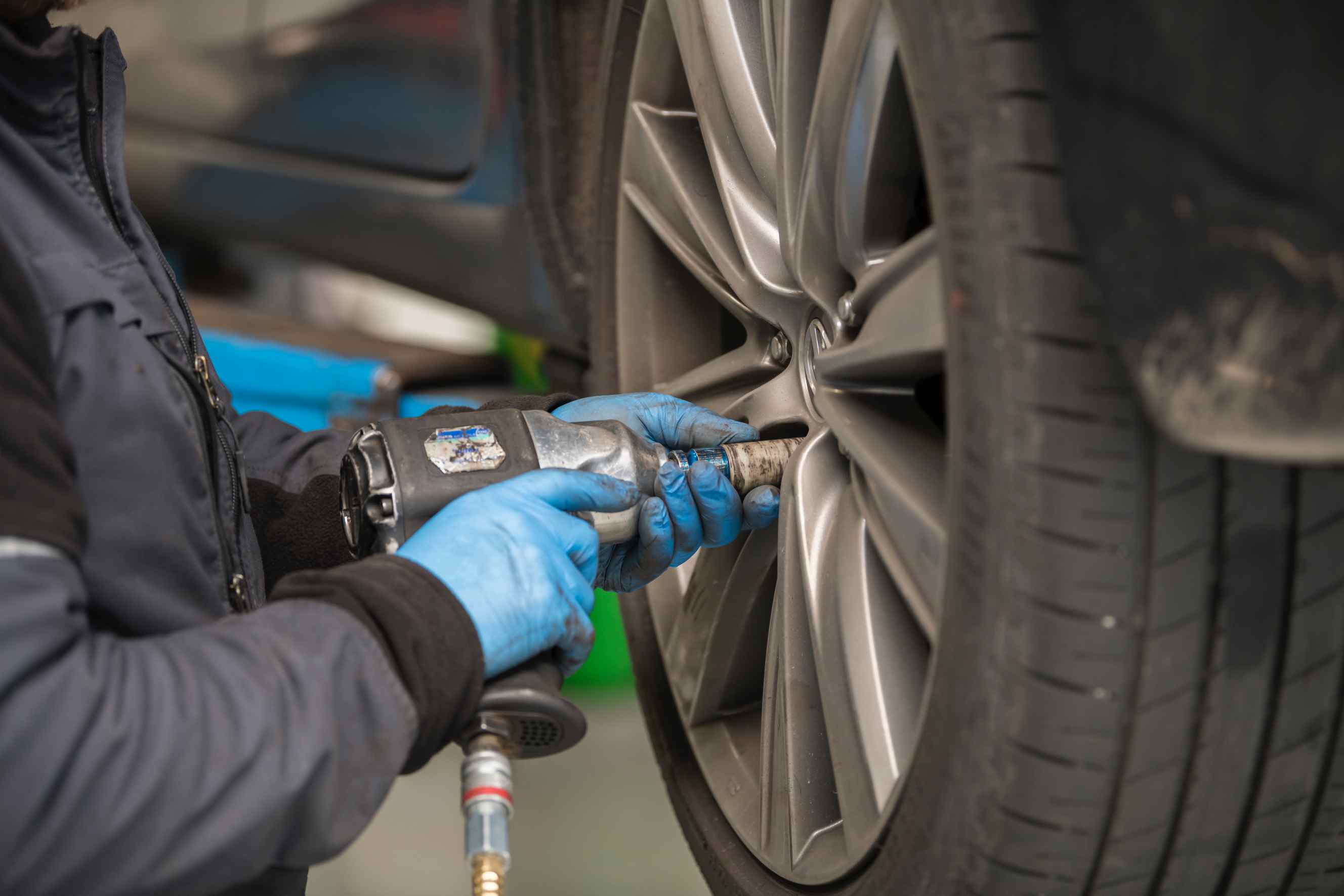 A mobile tyre fitter near you using a pneumatic impact wrench to tighten lug nuts on a car wheel during a tire service.
