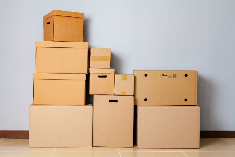 Pile of moving boxes against a light blue wall. - cardboard boxes vs plastic bins