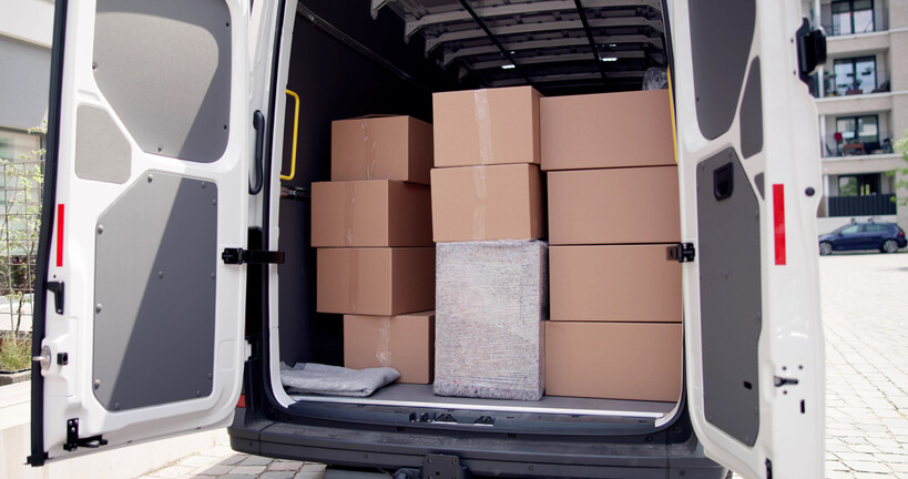 Open delivery van loaded with stacked cardboard moving boxes. - cardboard boxes vs plastic bins