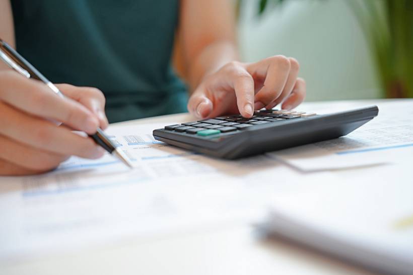 how to make money sewing - Close-up of a person using a calculator and pen to work on financial documents