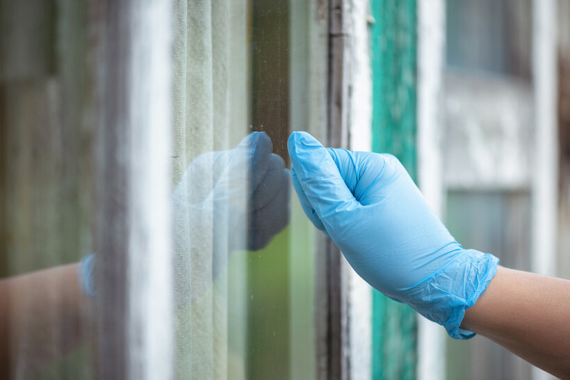 Hand in a blue glove inspecting a windowpane by tapping the glass. - aluminium vs upvc windows