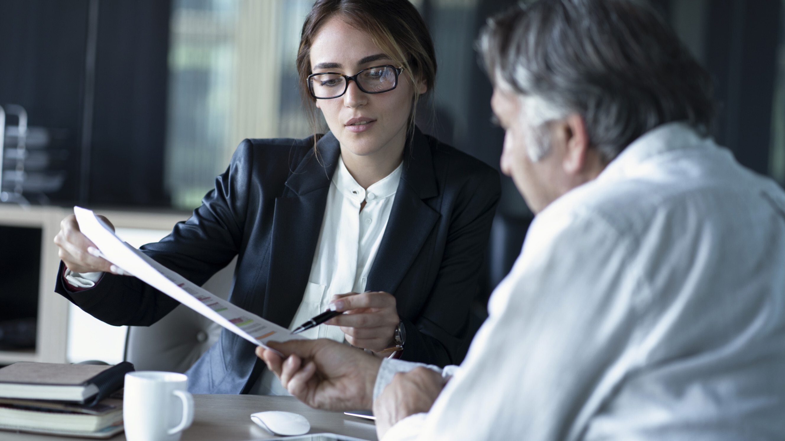 A young professional woman presenting a report to a mature male client across the table