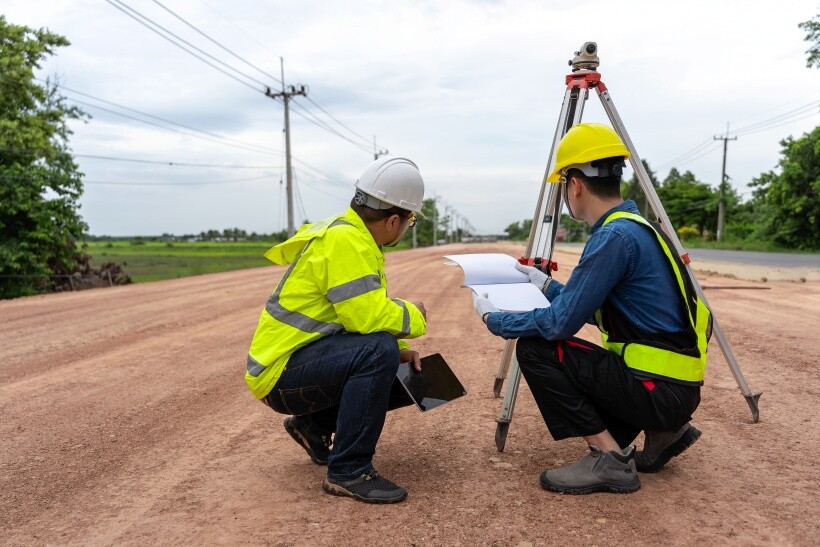 Building surveyors reviewing site plans and using surveying equipment