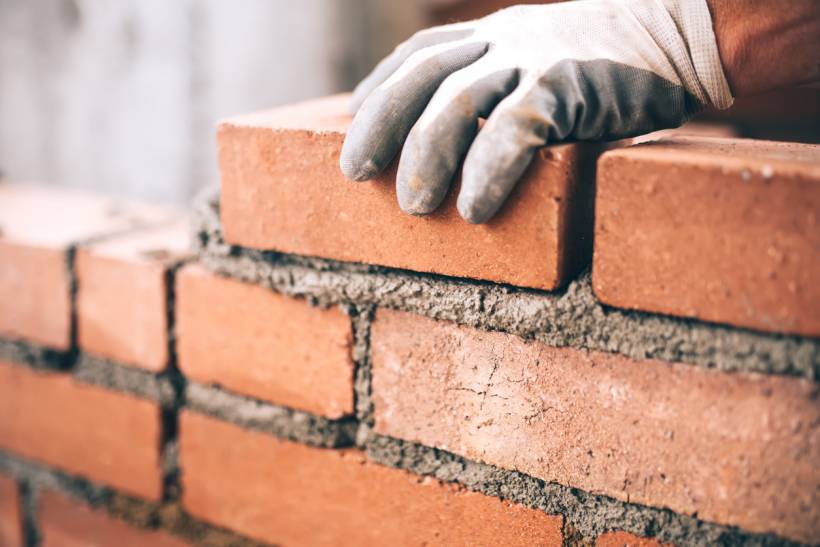 A gloved hand carefully placing a red brick onto a bed of mortar during construction. - lime mortar vs cement mortar