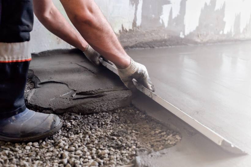 A worker in boots and gloves uses a tool to level fresh cement mortar over a gravel base. - cement mortar vs lime mortar