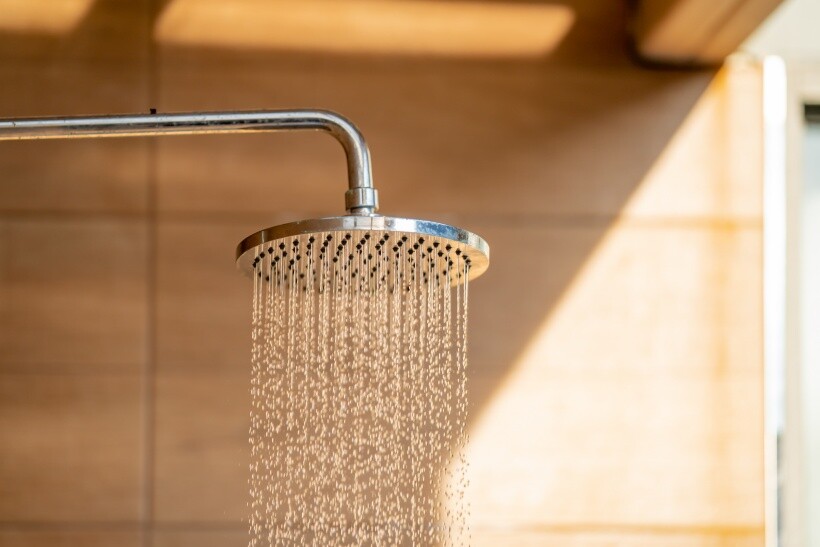 Power shower vs electric shower - Rain electric showerhead with running water in a warm-toned bathroom.