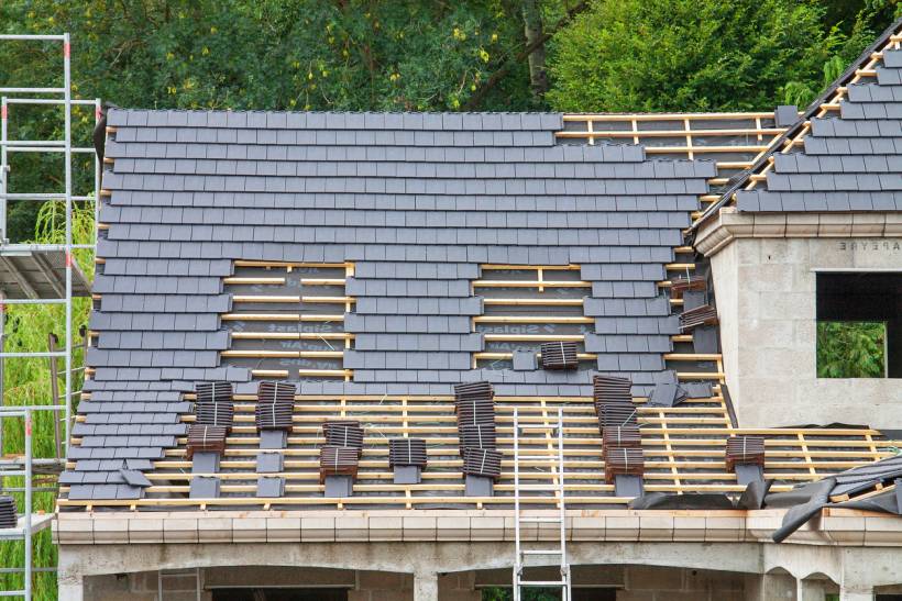 slate vs tile roof - Partially completed roof with dark shingles being installed on a house under construction