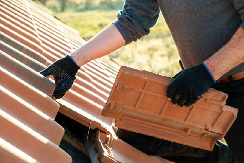 slate vs tile roof - Worker installing clay roof tiles on a sloped roof