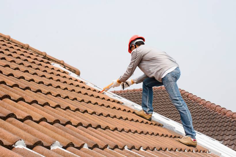 slate vs tile roof - Roof maintenance with a technician applying sealant to clay roof tiles
