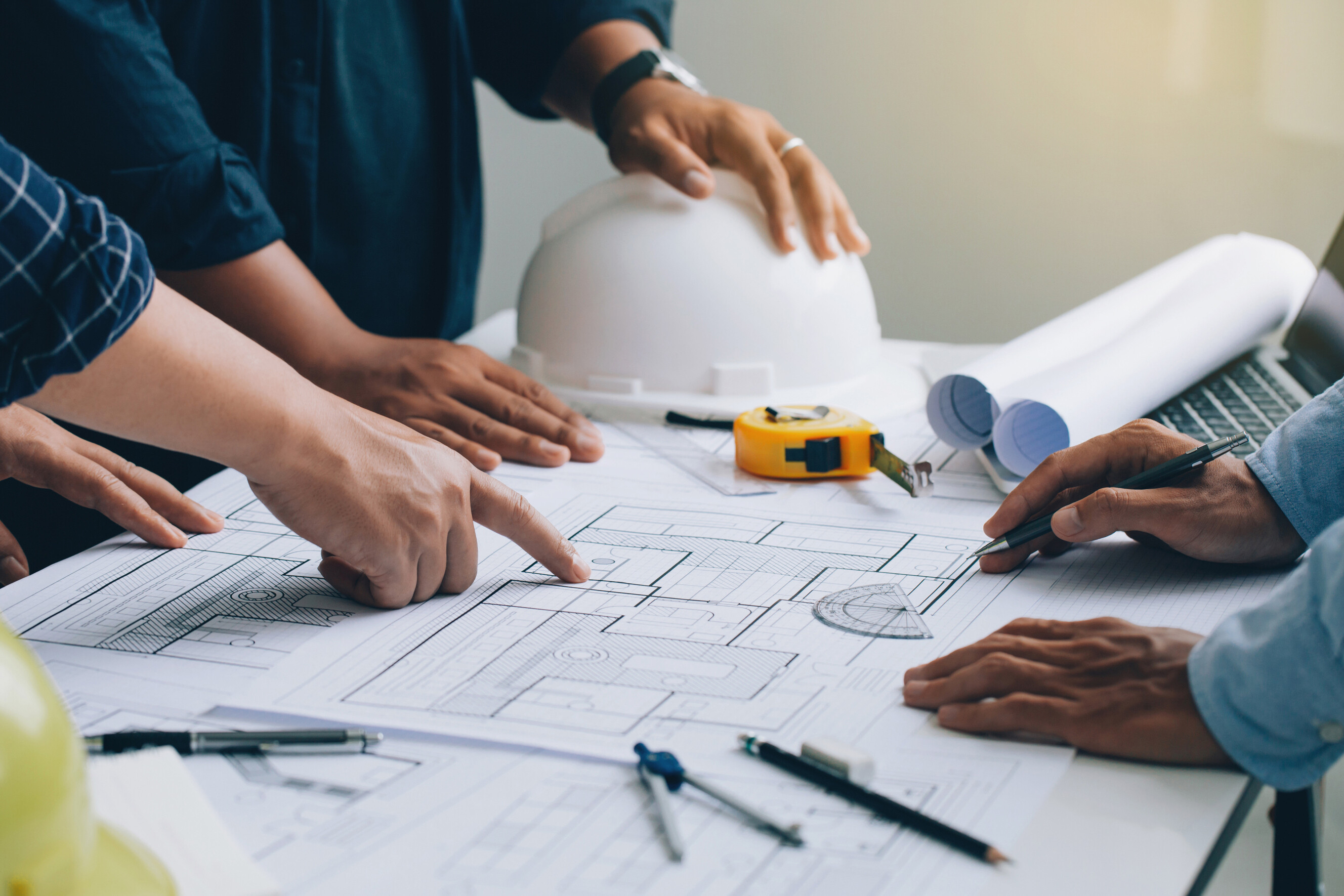 Group of architects reviewing blueprints on a table with tools and hard hats.