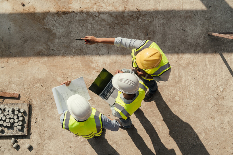 Aerial view of engineers in safety vests and helmets discussing a project layout. - architect vs engineer
