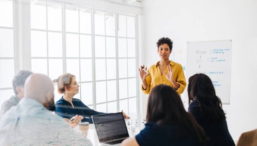 project manager vs product manager - Businesswoman leading a discussion with colleagues around a conference table