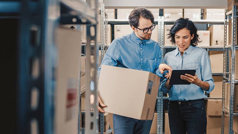 project manager vs product manager - Workers reviewing logistics information on a tablet inside a warehouse