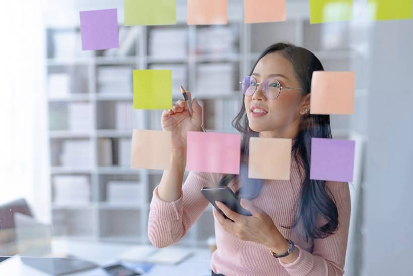 project manager vs product manager - Person organizing tasks using sticky notes for project management in an office