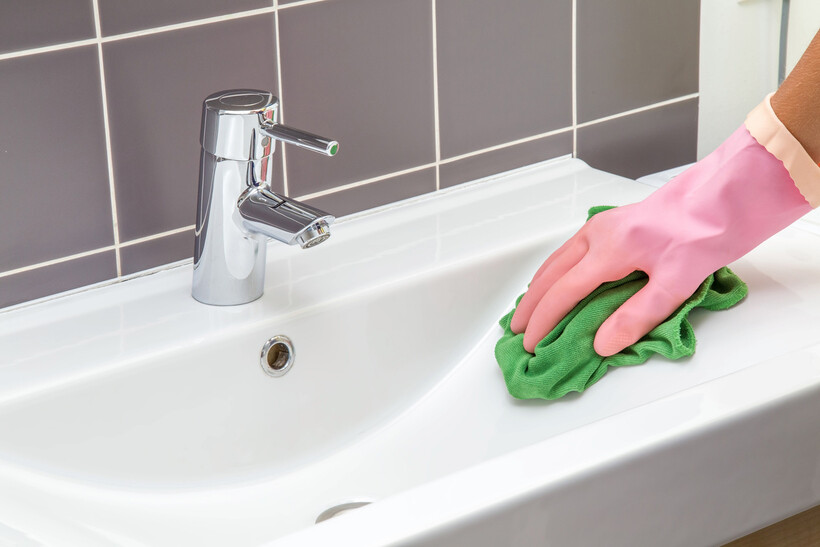 Person cleaning a white bathroom basin with a green cloth and pink gloves. - basin vs sink