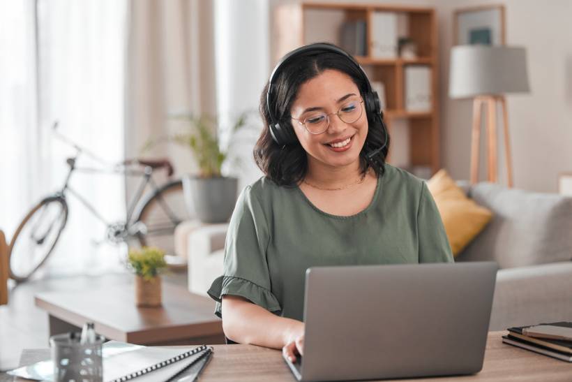 personal assistant vs virtual assistant - Virtual assistant working remotely on a laptop while wearing headphones