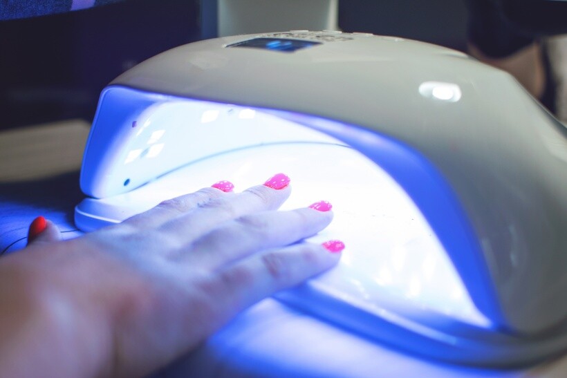 UV nail lamp vs LED nail lamp - Hand with bright pink nails curing under a LED nail lamp.