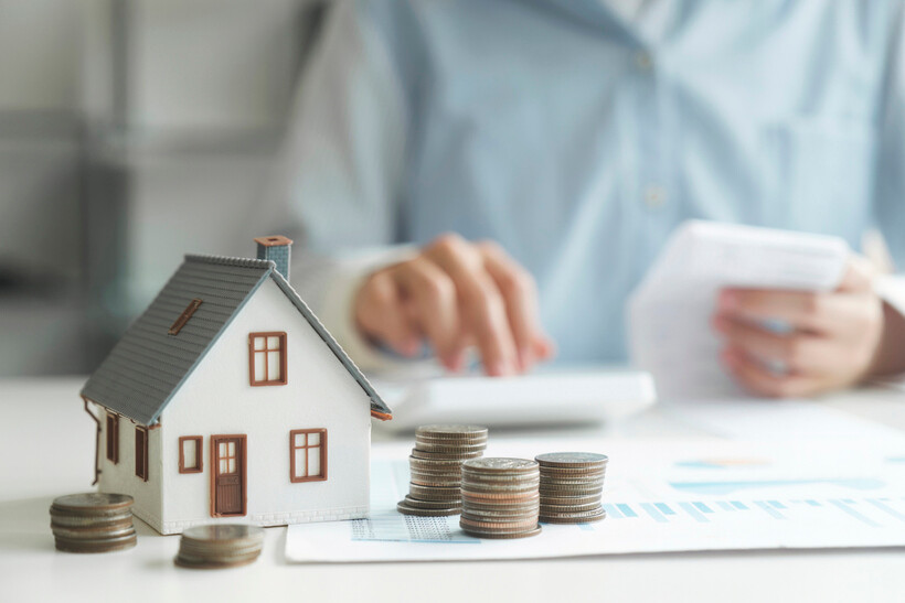 Person reviewing documents with house model and money stacks on a desk. - refurbishment vs renovation