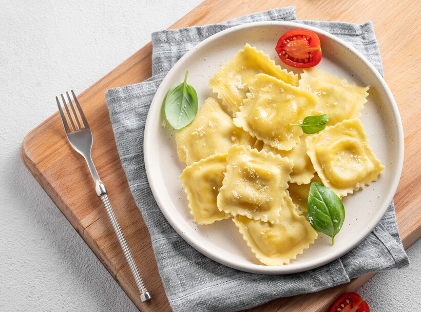 Italian ravioli pasta dish with herbs and tomato on a ceramic plate. - ravioli vs tortellini