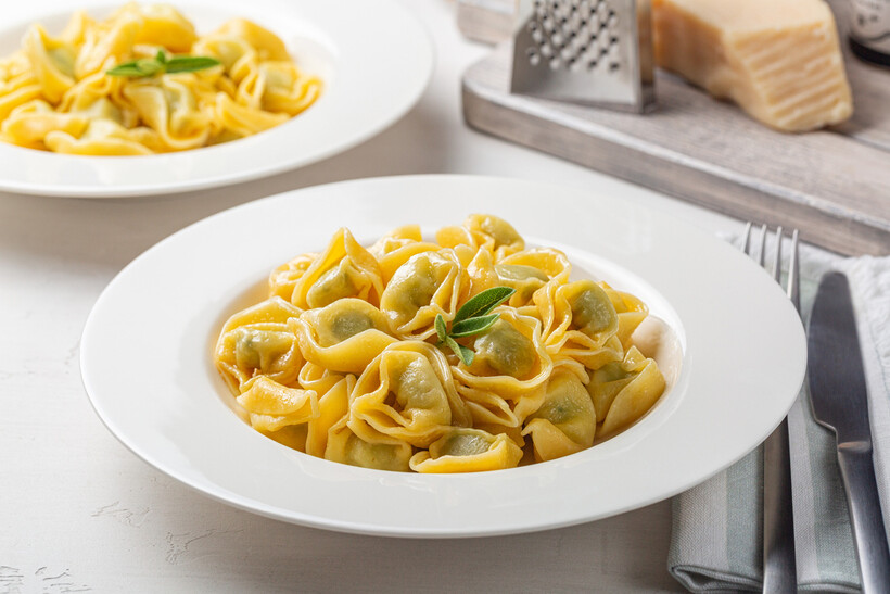Italian tortellini pasta dish presented in a white bowl with a garnish. - tortellini vs ravioli