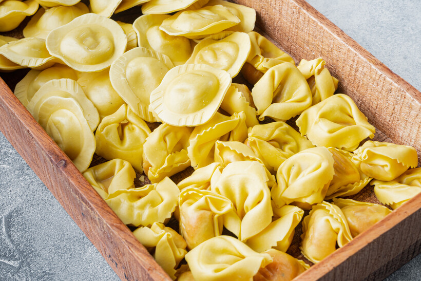 Wooden tray filled with uncooked ravioli and tortellini pasta. - ravioli vs tortellini
