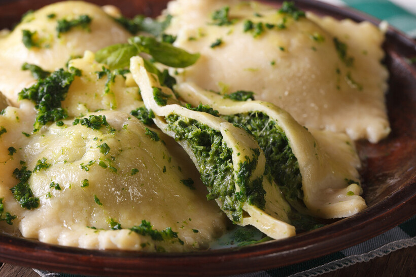Close-up of spinach and ricotta ravioli with herb sauce on a plate. - tortellini vs ravioli