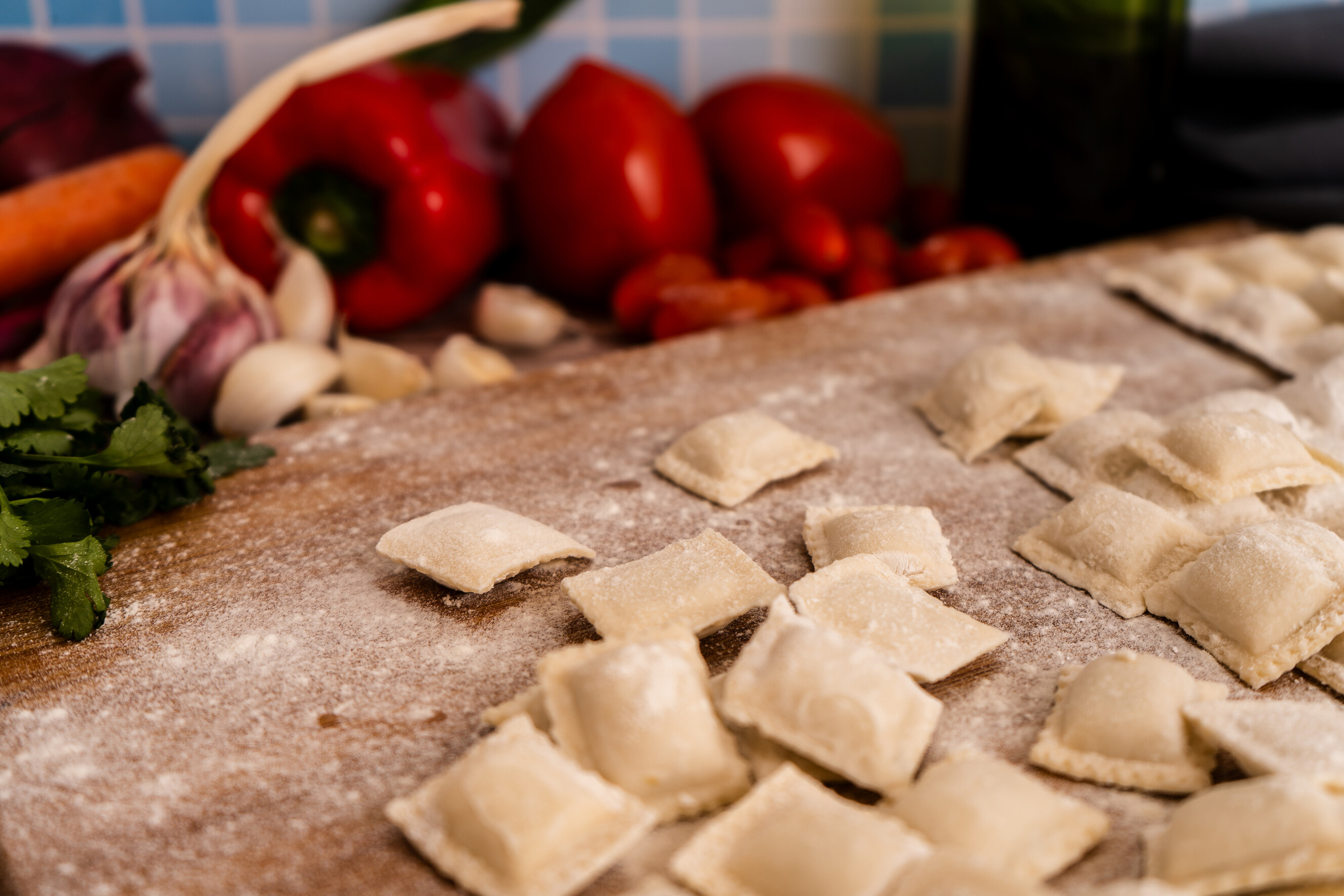 Homemade ravioli squares surrounded by garlic, tomatoes, and herbs.