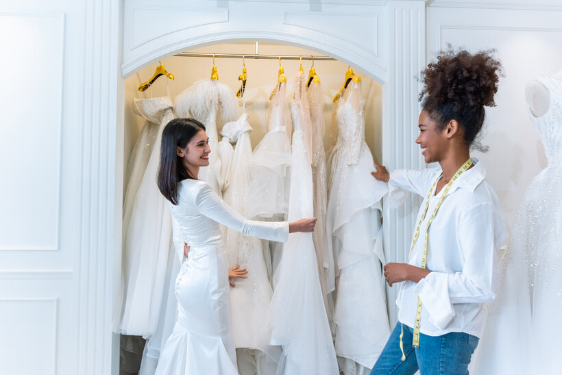 Bride and wedding planner selecting a gown among various wedding dresses. - wedding planner vs coordinator