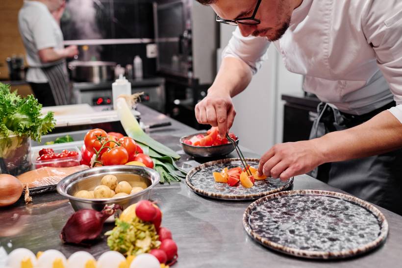 chef carefully plating sliced tomatoes in a professional kitchen - chef vs cook