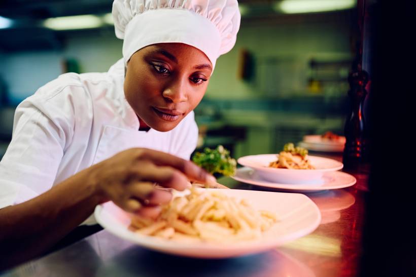 Female chef garnishing a plate of pasta in a professional kitchen. - cook vs chef