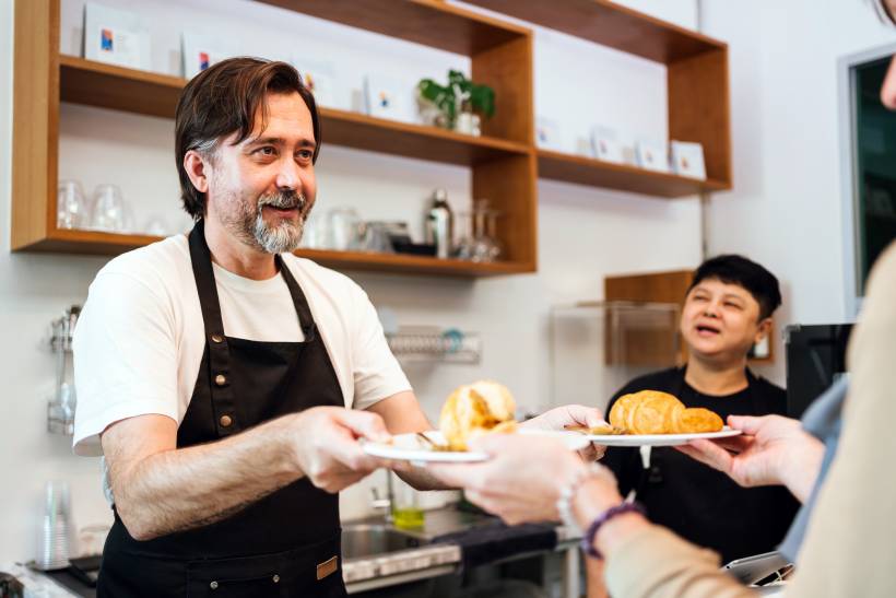 Male chef hands two plates of food to a customer across the counter. - chef vs cook