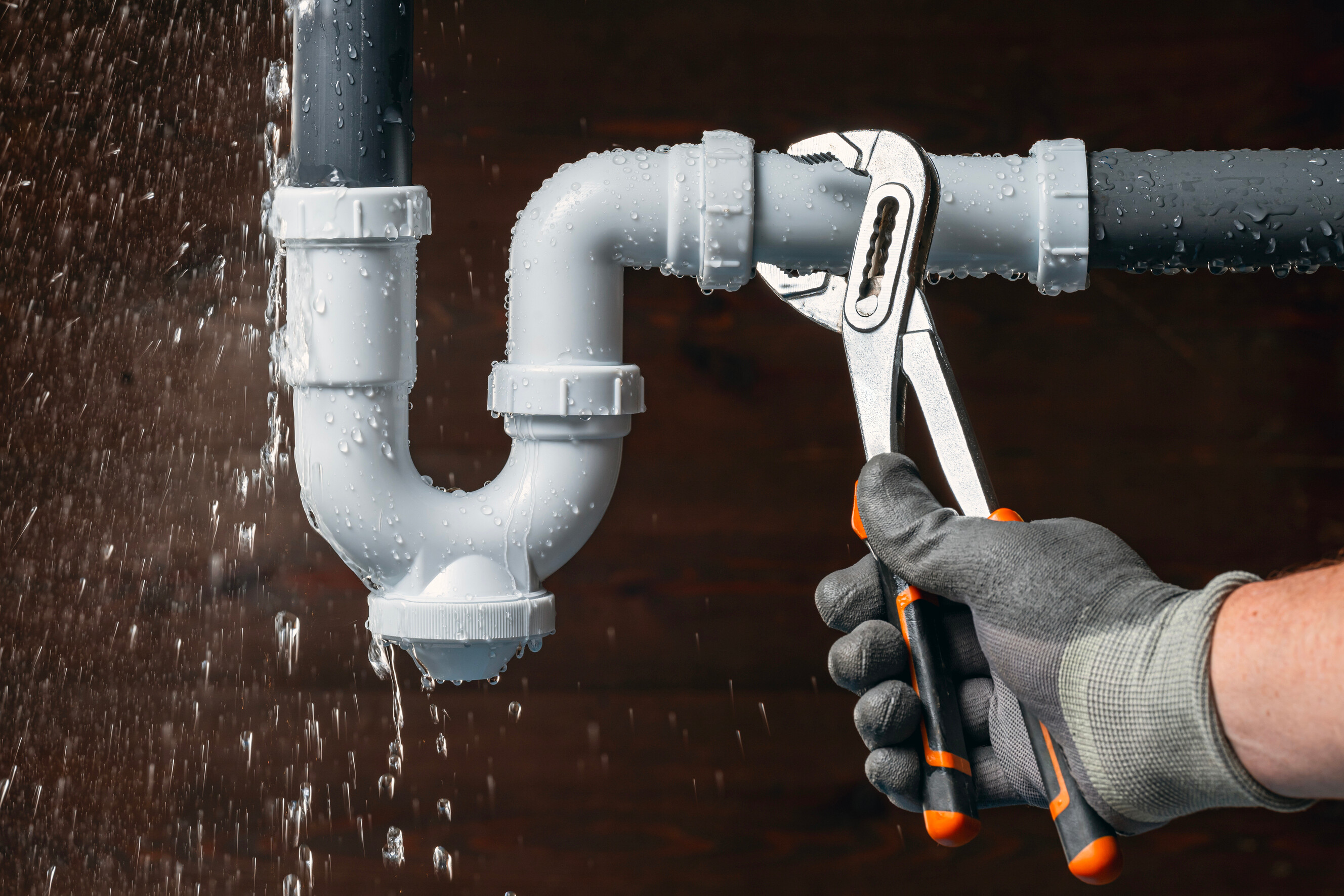 Plumber using a wrench to fix a leaking PVC pipe joint.