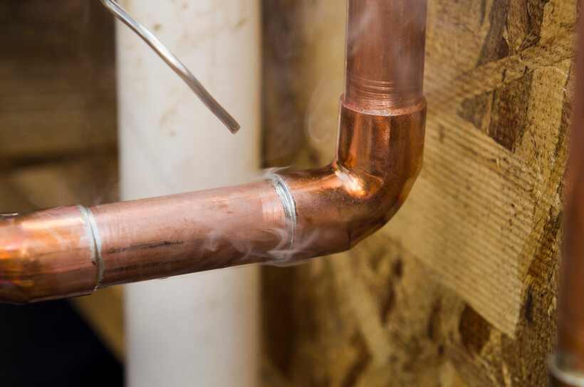 Close-up of hot copper pipe being welded near a wooden wall. - plastic pvc pipe vs copper pipe
