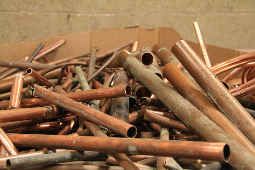 Assorted scrap copper pipes in a cardboard box against a concrete wall. - pvc pipe vs copper plumbing