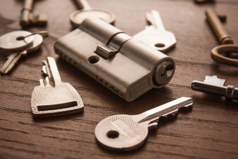 keysmith vs locksmith - Cylinder lock surrounded by various metal keys on a wooden surface