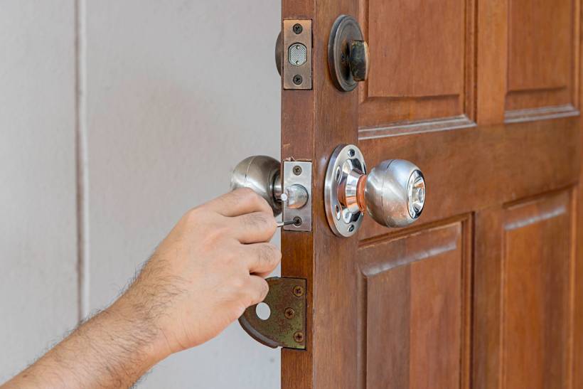 keysmith vs locksmith - Hand unlocking a wooden door with a key in a metal doorknob