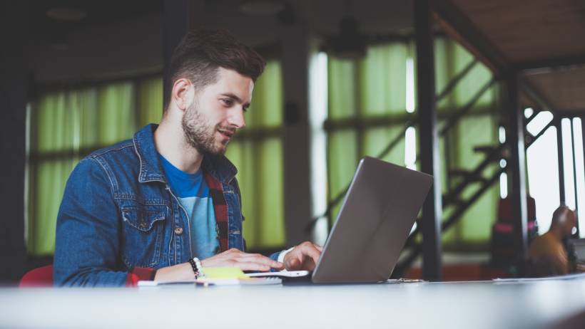 A young man with a beard concentrating on his laptop while working in an office. - web developer vs software developer