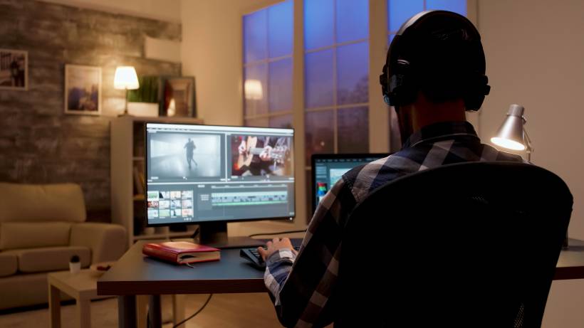 A video editor works late on a project, editing footage on his computer in a home office. - videographer vs cameraman