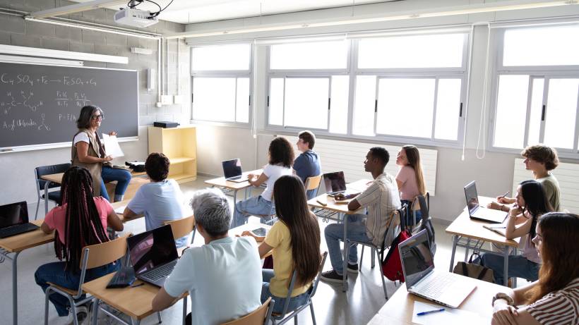 A teacher gives a lesson to her students who are seated at desks in a bright classroom - teacher vs tutor
