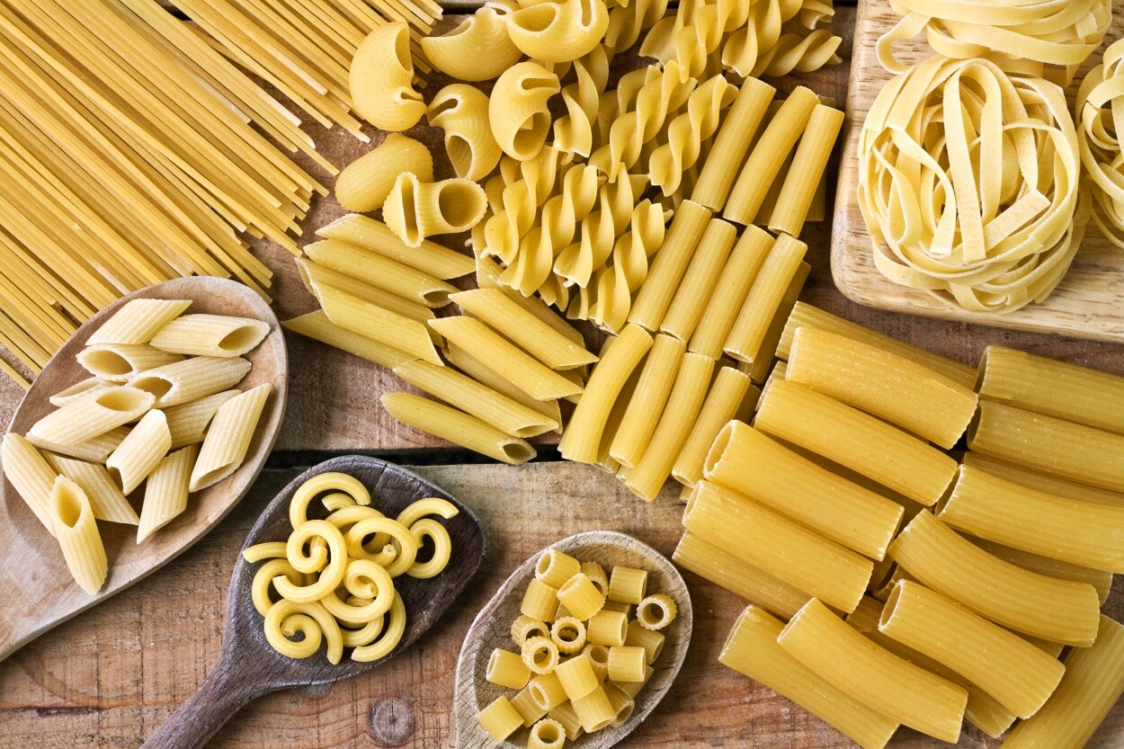 Collection of various pasta shapes laid out on a rustic surface