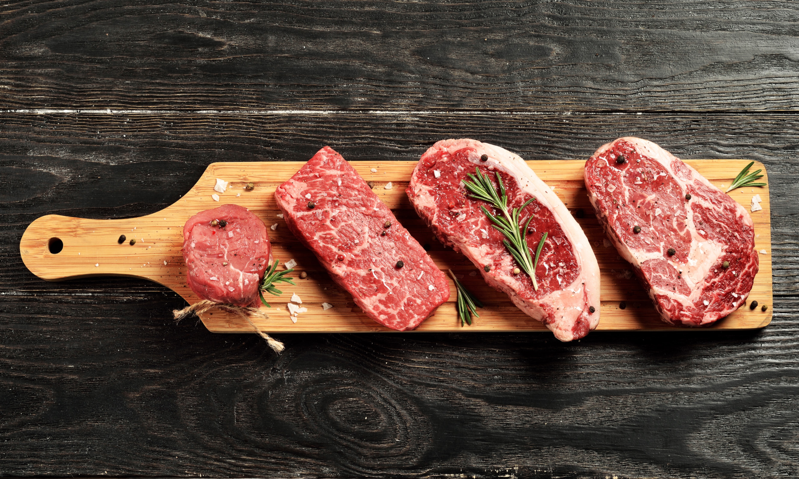 A side-by-side display of different steak cuts including porterhouse and scotch fillet on a wooden platter.