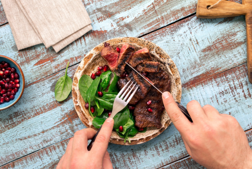 scotch fillet vs porterhouse - person cutting into a grilled steak served with spinach and pomegranate