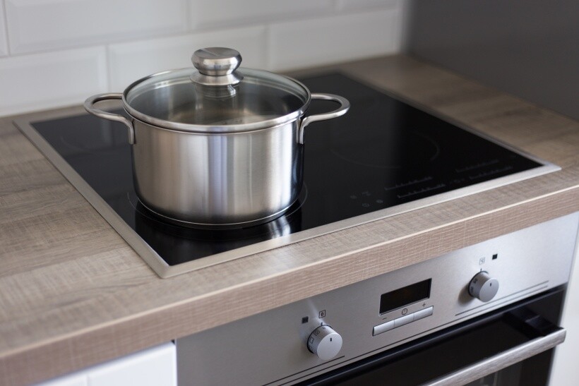 ceramic vs induction cooktop -Stainless steel pot on a ceramic glass cooktop above a built-in oven.