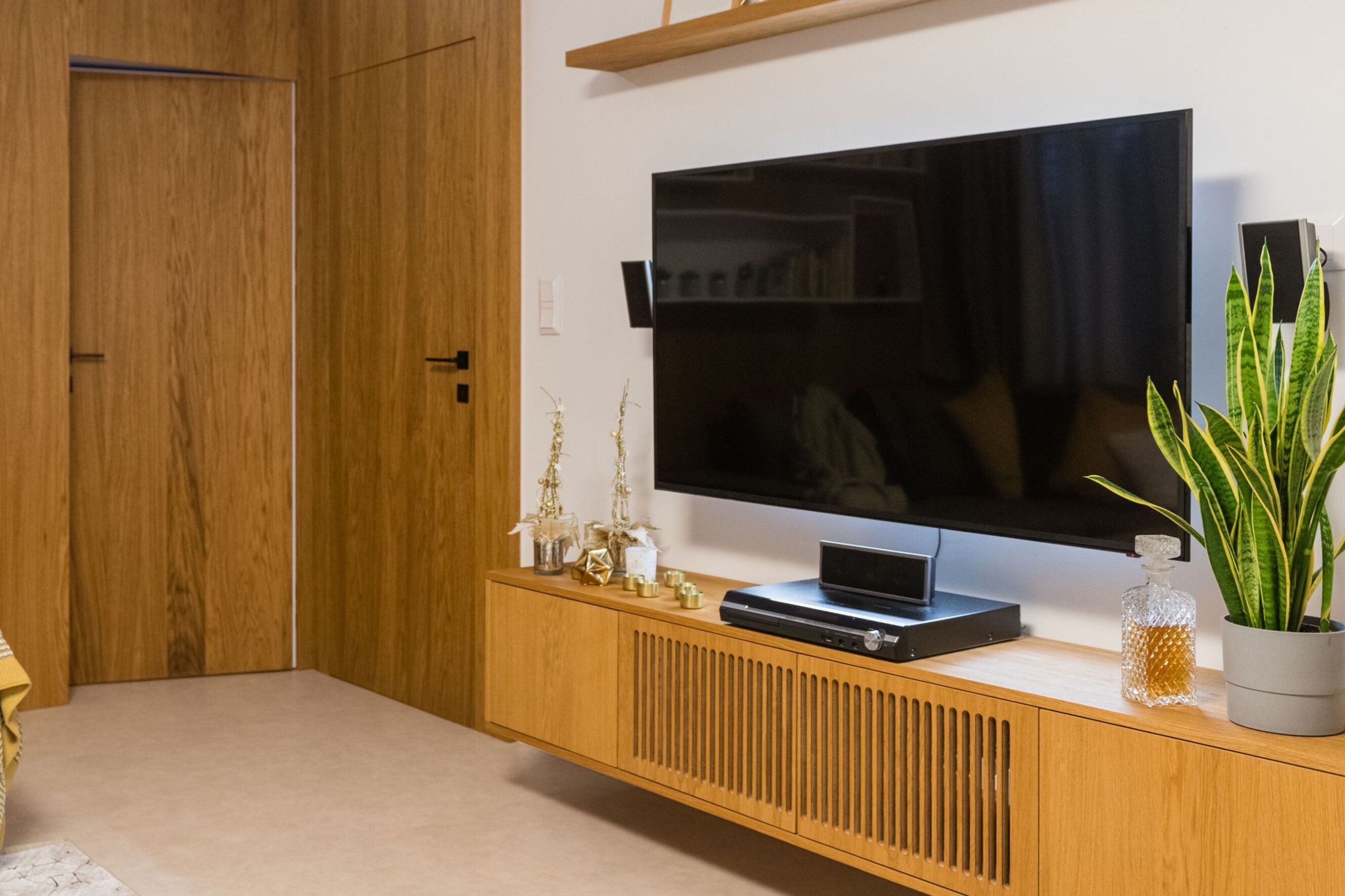 Flat-screen TV above a wooden cabinet with an indoor plant.