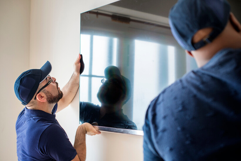 Workers unmounting a flat-screen TV on a wall. - how to pack a TV for moving