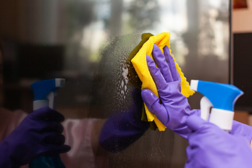 Close-up of hands in purple gloves wiping a TV screen. - how to pack a TV for moving