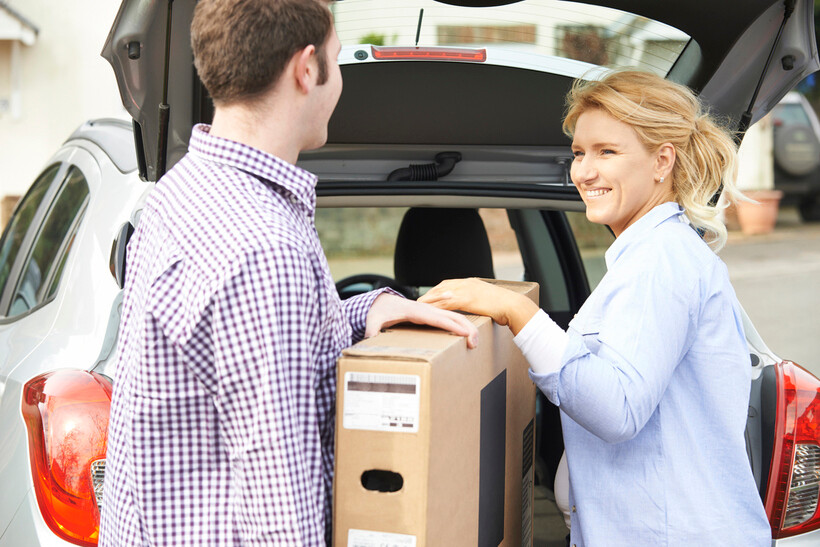 Two people loading a boxed TV into the back of a vehicle. - how to pack a TV for moving